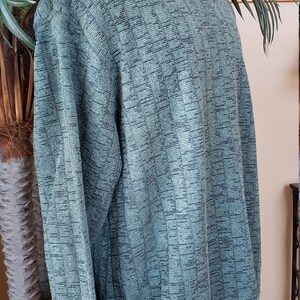 May include: A green long-sleeved sweater with a ribbed texture. The sweater has a crew neck and a ribbed hem.