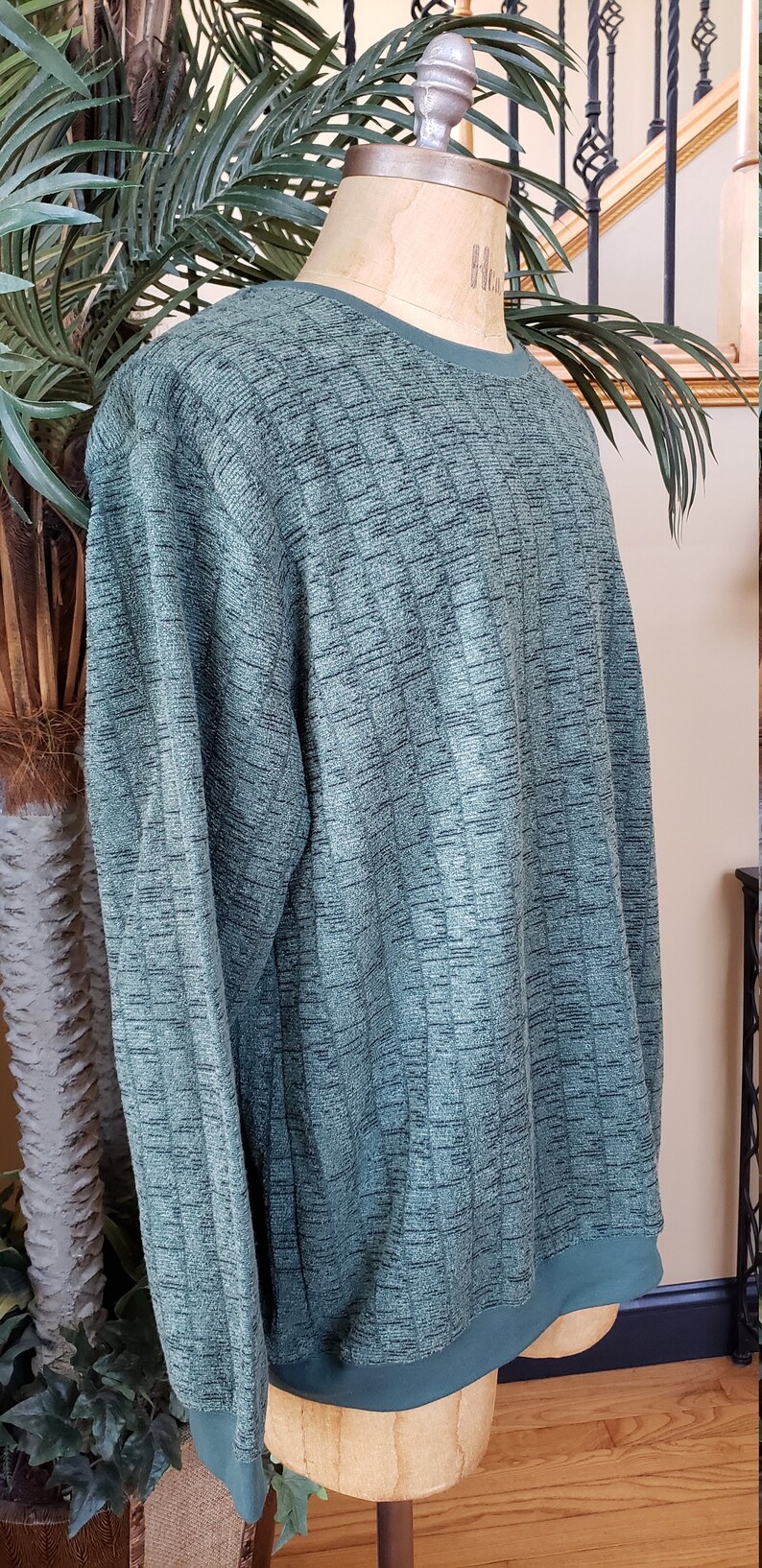 May include: A green long-sleeved sweater with a ribbed texture. The sweater has a crew neck and a ribbed hem.