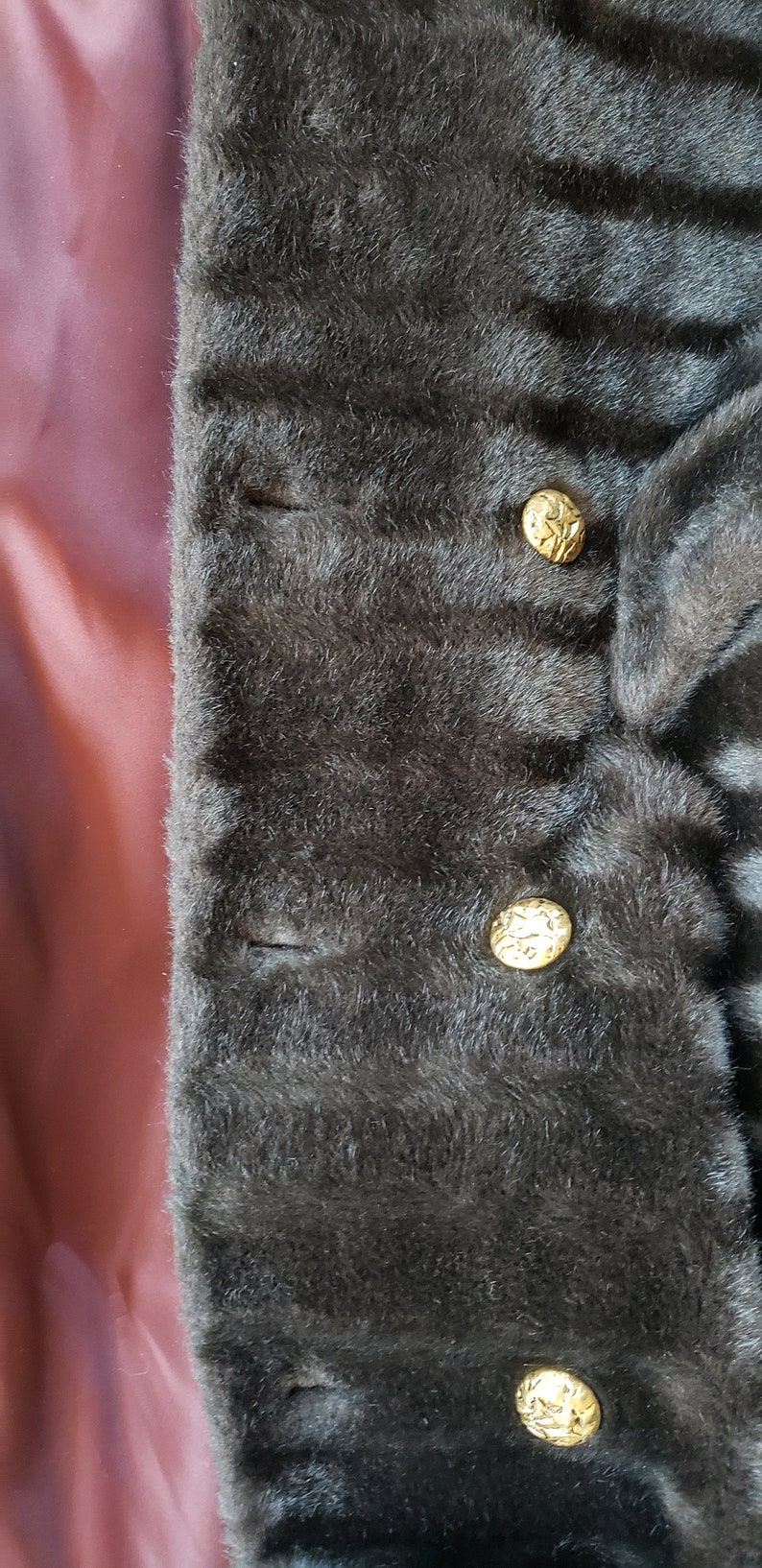 Puede incluir: Primer plano de una chaqueta de piel sint&eacute;tica marr&oacute;n oscuro con tres botones dorados. Los botones tienen un dise&ntilde;o decorativo.