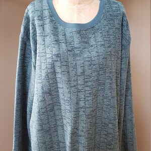 May include: A green long-sleeved sweater with a textured pattern. The sweater has a round neckline and a ribbed hem.