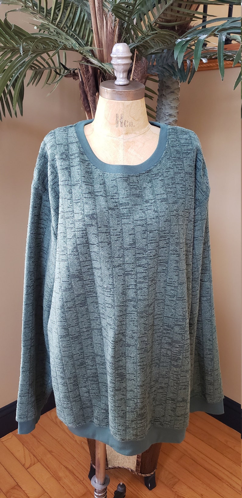 May include: A green long-sleeved sweater with a textured pattern. The sweater has a round neckline and a ribbed hem.