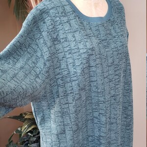 May include: A teal green sweater with a textured knit pattern. The sweater has a round neckline and long sleeves.