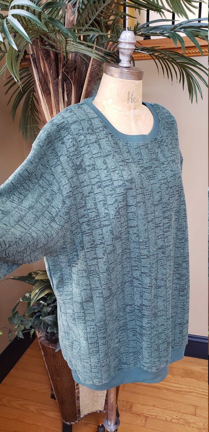 May include: A teal green sweater with a textured knit pattern. The sweater has a round neckline and long sleeves.