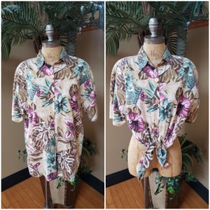 May include: A short-sleeved button-down shirt with a tropical print featuring brown, green, and pink flowers on a beige background. The shirt is tied at the waist.