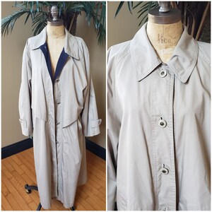 May include: A beige trench coat with a button closure and a black lining. The coat has a collar and long sleeves.