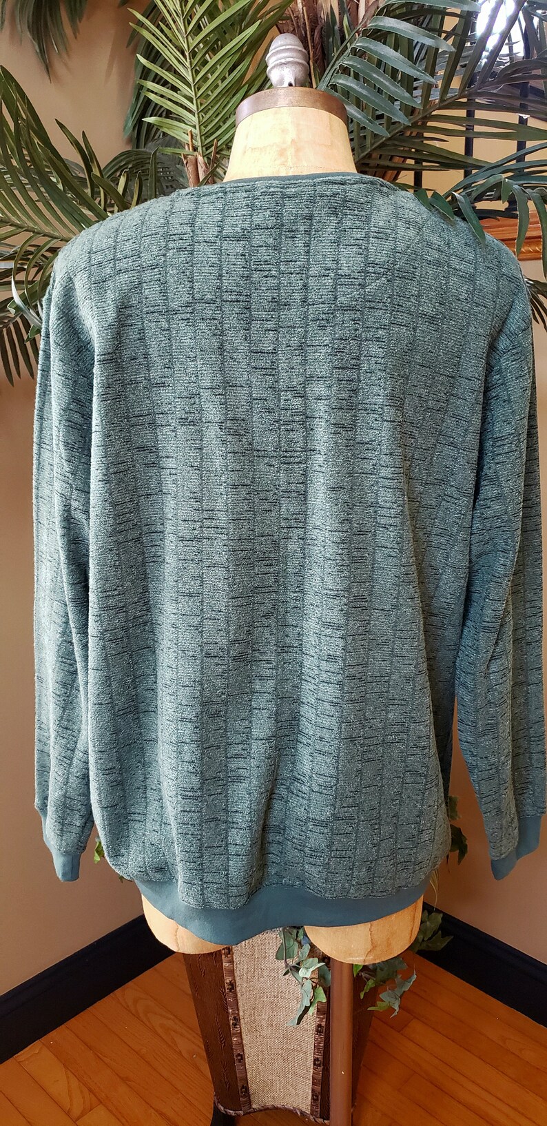 May include: A green long-sleeved sweater with a textured pattern. The sweater is on a mannequin.