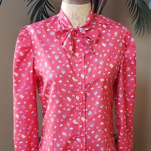 May include: A red long-sleeved blouse with a small floral print and a bow tie at the neck.