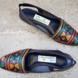 May include: A pair of black leather slip-on shoes with a colorful geometric pattern on the toe. The shoes have a Liz Claiborne label on the insole.