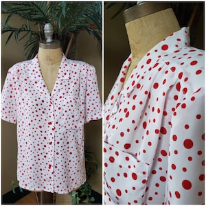 May include: White short-sleeved button-down shirt with a red polka dot pattern. The shirt has a chest pocket and a classic collar. The shirt is displayed on a mannequin.