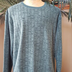 May include: A green long-sleeved sweater with a textured pattern. The sweater has a crew neck and a ribbed hem.