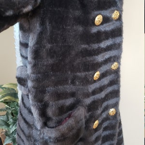 Puede incluir: Una chaqueta de piel sint&eacute;tica marr&oacute;n oscuro con un patr&oacute;n a rayas y botones dorados. La chaqueta tiene un cuello y un bolsillo en el lado izquierdo.
