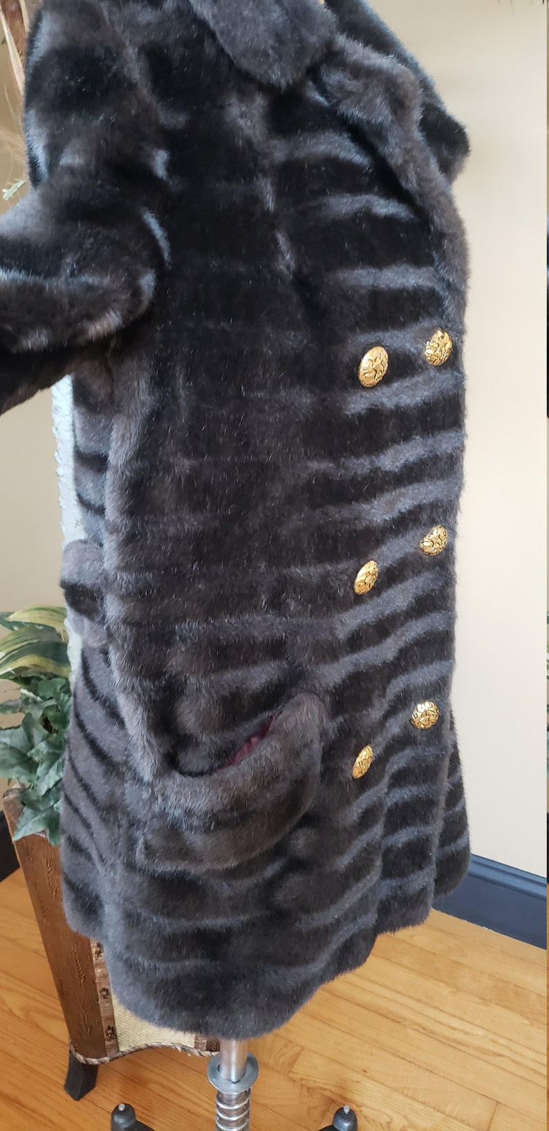 Puede incluir: Una chaqueta de piel sint&eacute;tica marr&oacute;n oscuro con un patr&oacute;n a rayas y botones dorados. La chaqueta tiene un cuello y un bolsillo en el lado izquierdo.