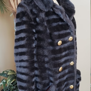 Puede incluir: Una chaqueta de piel sint&eacute;tica negra con un patr&oacute;n a rayas y botones dorados. La chaqueta tiene un cuello y dos bolsillos.