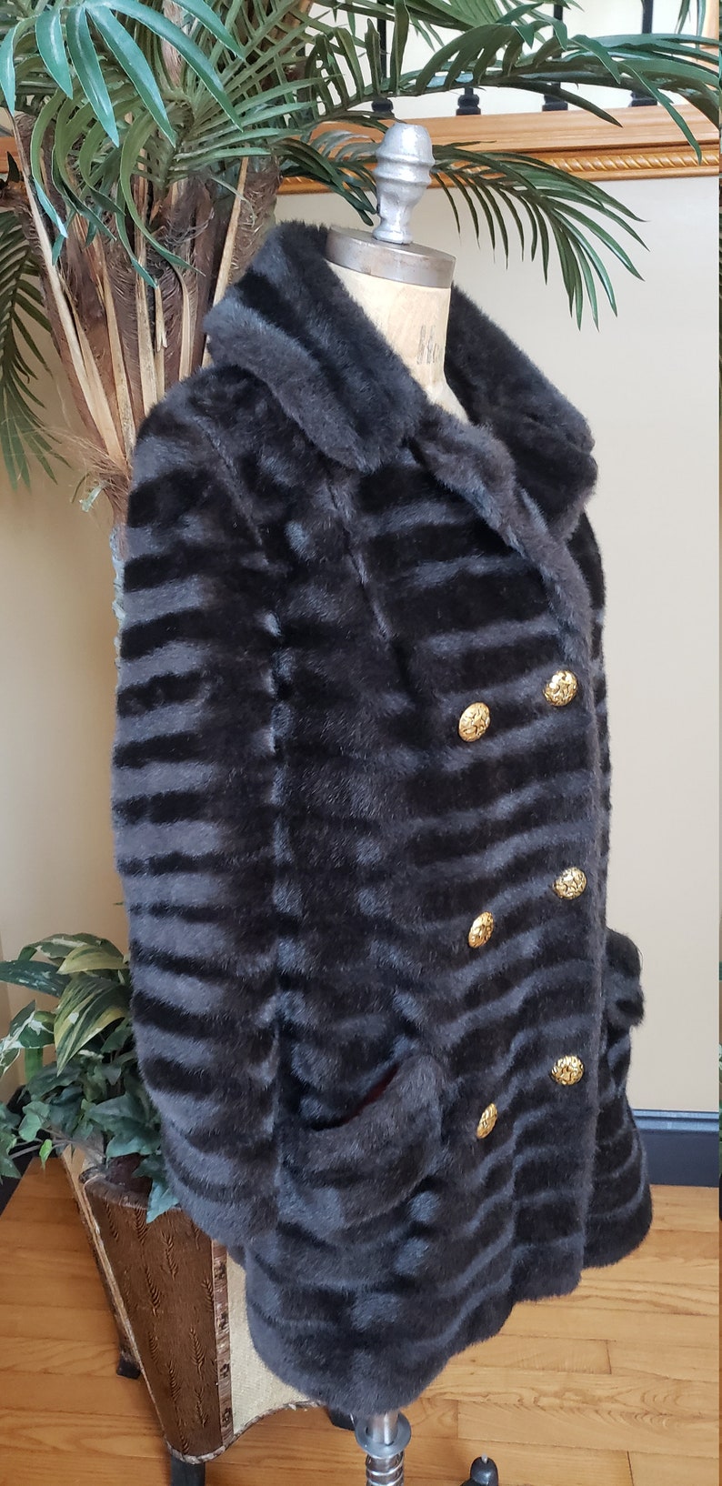Puede incluir: Una chaqueta de piel sint&eacute;tica negra con un patr&oacute;n a rayas y botones dorados. La chaqueta tiene un cuello y dos bolsillos.