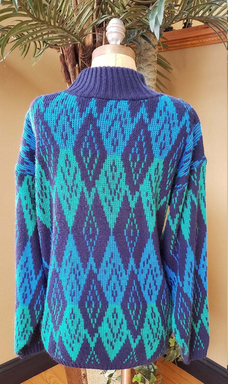 May include: A blue and green patterned sweater with a high neck. The sweater is made of a soft, knitted fabric.