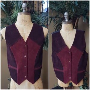 May include: A burgundy suede vest with a contrasting dark brown suede panel on the front. The vest has a V-neckline and a button closure.