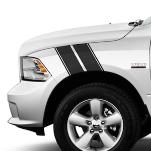 May include: A white truck featuring black and white racing stripes on the front wing. The stripes are angled and parallel, with a thin white stripe between two thick black stripes. The truck has a black tyre and a silver alloy wheel.