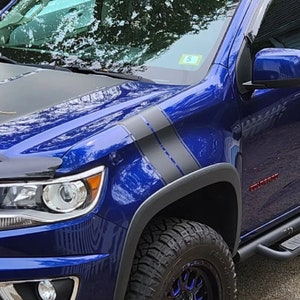 May include: A blue pickup truck with black racing stripes on the side. The truck has a black bonnet and a black bumper. The truck has a black step bar and black wheels.