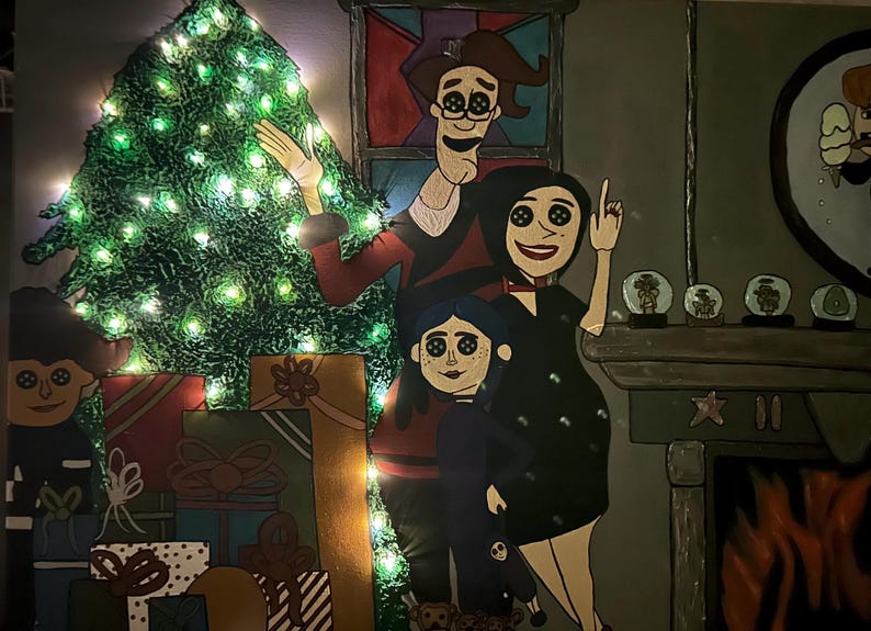 Op de afbeelding: Een grillig kerstkunstwerk met een familie met knoogogen, een versierde kerstboom met lichtjes en ingepakte cadeaus. Het kunstwerk heeft een open haard en een ronde spiegel met een stel.