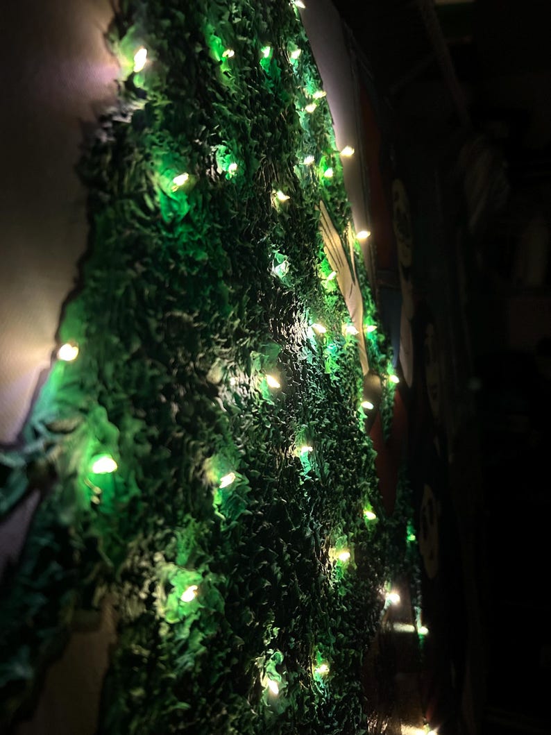 Op de afbeelding: Een groene muur met textuur en ingebouwde lichten. De muur heeft een ruw, ongelijkmatig oppervlak en de lichten zijn klein en gelijkmatig verdeeld, waardoor een zachte, warme gloed ontstaat. Het algehele effect is een decoratieve, verlichte display.