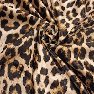 May include: Close-up of a brown and black leopard print fabric. The fabric is soft and has a subtle sheen.