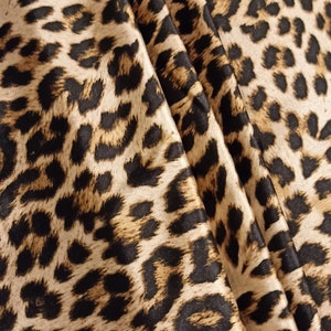 May include: Close-up of a brown and black leopard print fabric with a satin finish. The fabric is folded and draped, showing the texture and pattern.