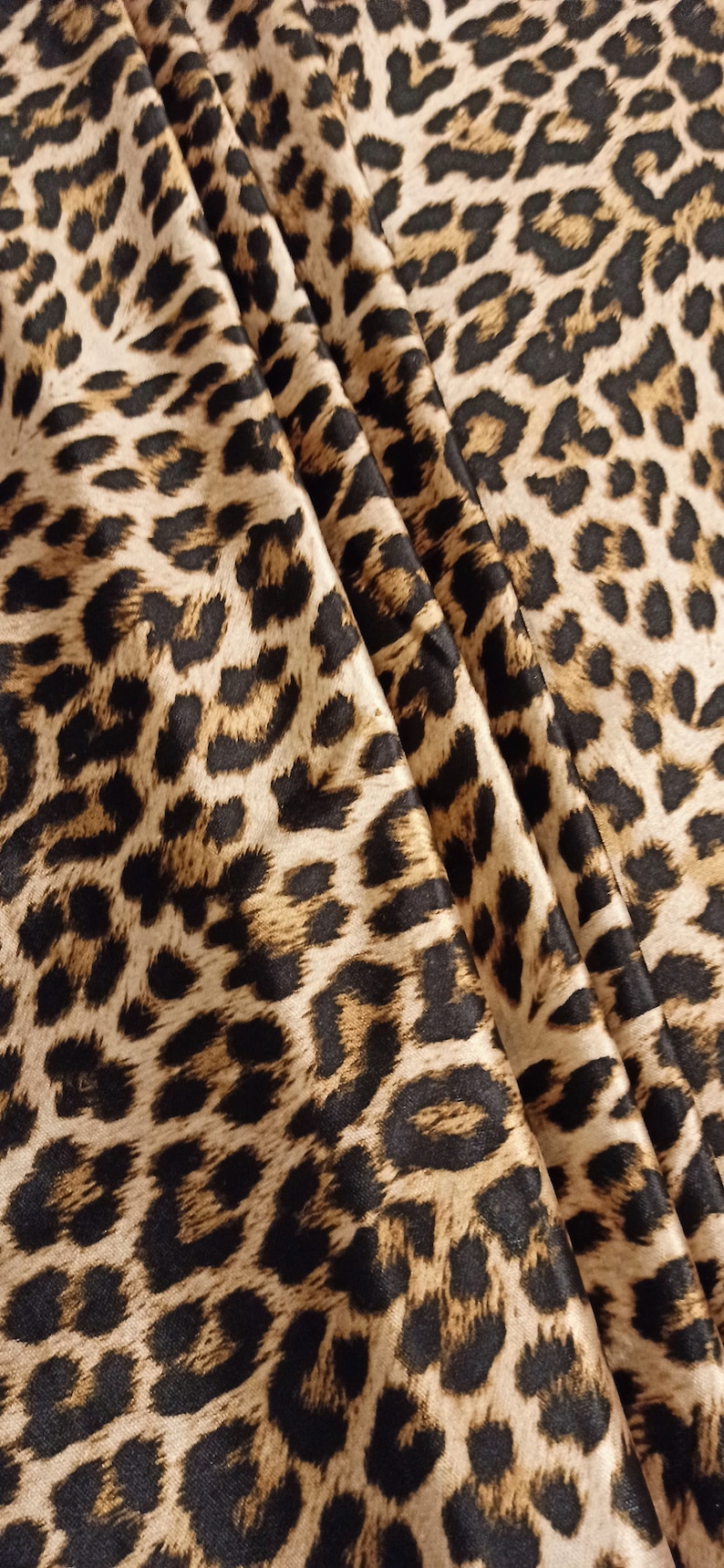 May include: Close-up of a brown and black leopard print fabric with a satin finish. The fabric is folded and draped, showing the texture and pattern.