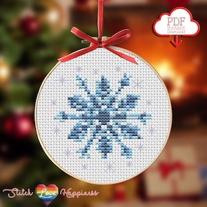 May include: A blue and white snowflake cross stitch pattern on a white background. The pattern is in a round wooden embroidery hoop. The hoop is hanging from a red ribbon. The text "Stitch Love Happiness" is at the bottom of the image.