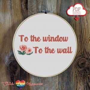 以下が含まれることがあります： 「To the window, To the wall」の文字がサンゴ色の糸で刺繍されたクロスステッチの刺繍枠。花のモチーフもあしらわれています。デザインは白い布の背景にあり、木の枠で囲まれています。「PDF Instant Download」と書かれた赤い雲のグラフィックが右上隅にあります。