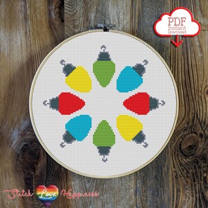 May include: A cross stitch pattern featuring a circle of colorful light bulbs. The pattern is displayed on a white embroidery hoop.