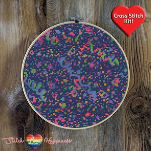 Peut inclure: Un kit de point de croix avec un motif abstrait coloré sur fond bleu foncé. Le motif est dans un cercle de broderie rond. Le texte "Cross Stitch Kit!" est dans un cœur rouge.