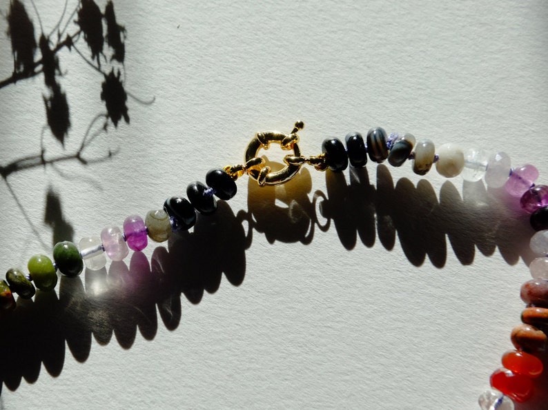 17 inches gemstone candy necklace strung on lilac silk. Agate, amazonite, apatite, citrine, fluorite, jade, jasper, labradorite, onyx, unakite, and quartz are used. There is a knot between each stone and finished with a 14k gold filled bold clasp