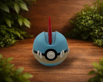 May include: A spherical toy featuring a light blue top half and a tan bottom half, separated by a black band with a central circular button. A prominent red fin-like protrusion extends from the top, and white claw-like accents flank the center.