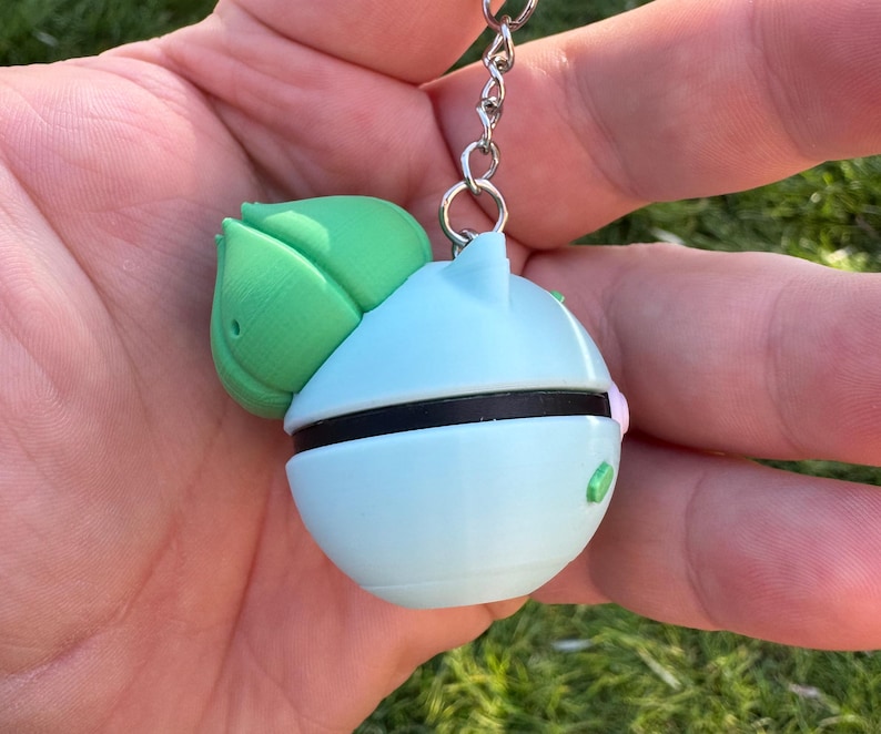 May include: A light blue and green keychain featuring a round design with a black band and a green leaf-like shape. The keychain is attached to a silver metal chain.