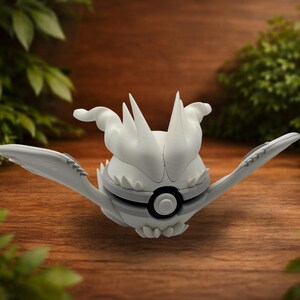 May include: A white spherical creature figurine with pointed spikes on top, two wide wing-like appendages extending to the sides, and a circular black and white emblem on the front center, resembling a stylized ball with organic features.