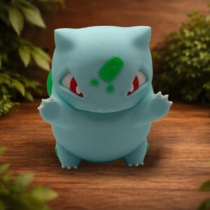 May include: A light blue creature figurine with a rounded body, pointed ears, and small white claws. The figure features red eyes and green textured patches on its forehead and back, standing in a forward-facing pose with arms outstretched.