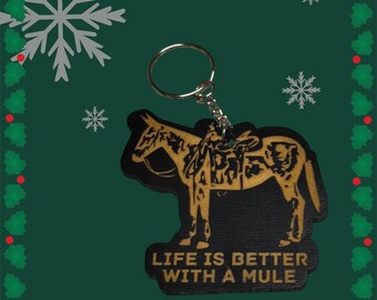 May include: A wooden keychain with a black silhouette of a mule with a saddle and the text "Life is better with a mule".