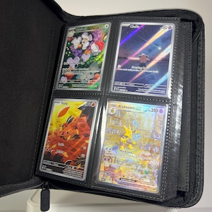 May include: A black zippered trading card binder filled with four Pok&eacute;mon cards. The cards feature colorful illustrations of various Pok&eacute;mon characters, including Cleffa, Tepig, and Alakazam. The binder is open, displaying the cards in clear plastic sleeves.