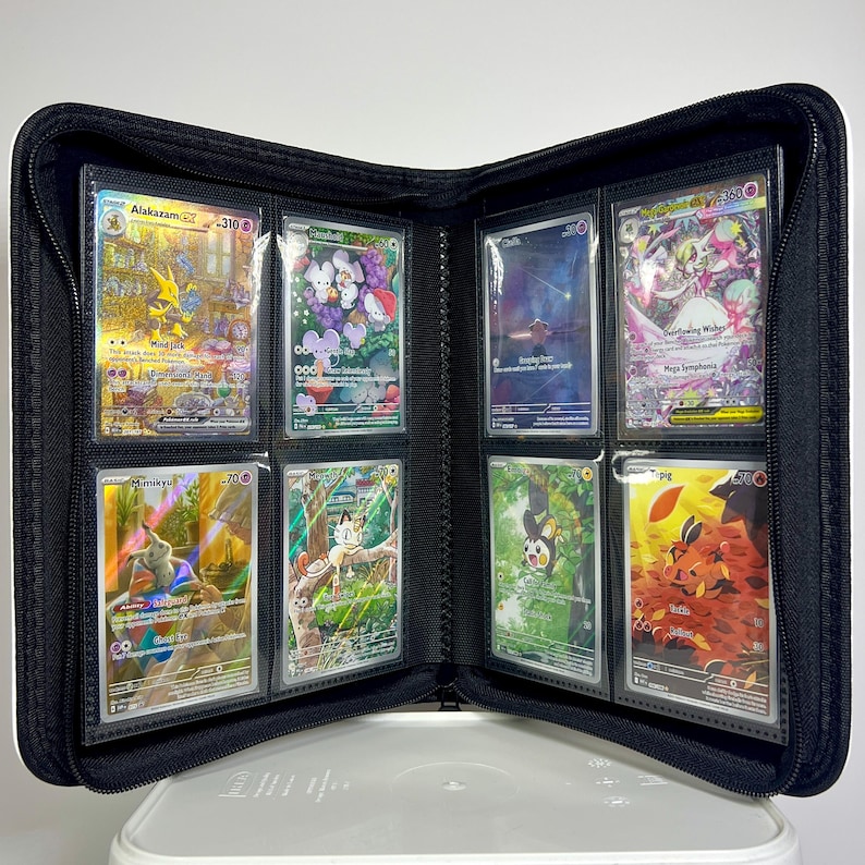 May include: Black zippered binder open to display trading cards. The cards are in clear sleeves and feature colorful illustrations of various characters. The binder is on a white surface.