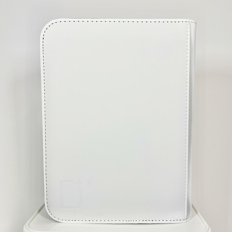 May include: A white, rectangular, leather-bound portfolio with rounded corners. The cover features a stitched border and a subtle embossed design in the lower left corner. The portfolio is sitting on a white surface.