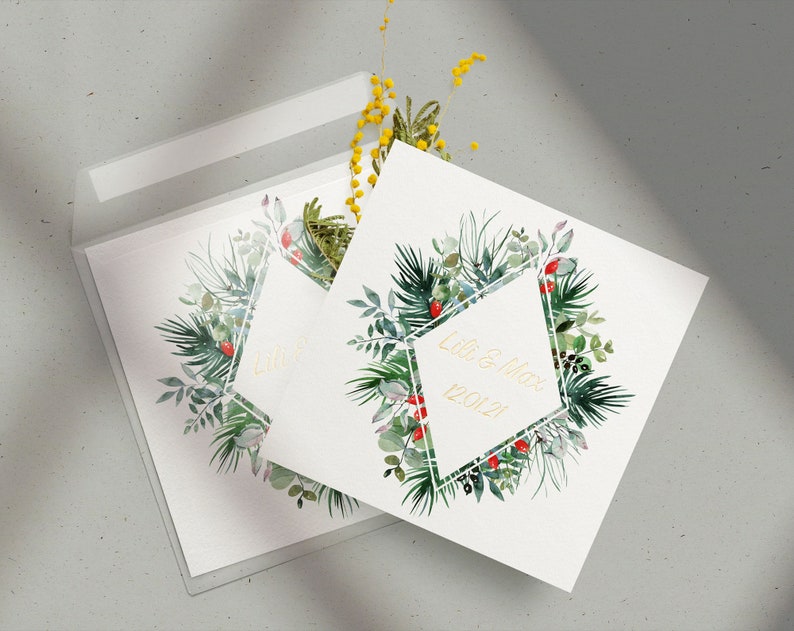 Op de afbeelding: Twee witte kaarten met een groen en rood bloemenontwerp en een gouden geometrisch frame. De tekst "Lori & Max 12.01.2021" staat op een kaart binnen het frame.