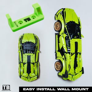 Könnte beinhalten: Ein grünes Lego Lamborghini Modell mit schwarzen Akzenten und goldenen Rädern. Das Modell ist mit einem grünen Kunststoff-Wandhalter an einer Wand befestigt. Der Wandhalter hat den Text "TB" aufgedruckt. Das Bild enthält den Text "EASY INSTALL WALL MOUNT".
