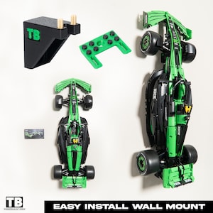 May include: A green and black Formula 1 race car wall mount with the words "Kick" and "TB" on it. The mount is made of plastic and has a simple design. It comes with a set of mounting hardware for easy installation.