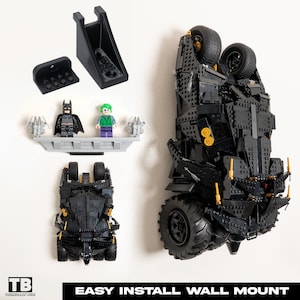 May include: Black Lego Batman Batmobile wall mount with two Lego minifigures, Batman and the Joker. The mount is made of black plastic and has a simple design. The Batmobile is upside down and the minifigures are standing on a small platform.