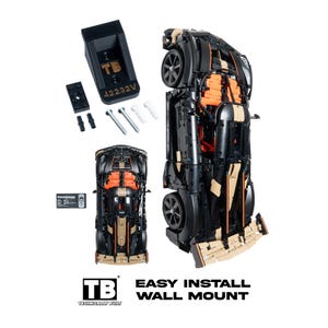 May include: A black and tan model car with orange interior details, accompanied by a black wall mount bracket labeled TB 42232V, two screws, two wall anchors, two black pins, and a small black plaque with the text Koenigsegg and Easy Install Wall Mount.