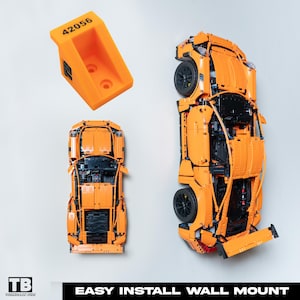 May include: Orange Lego Porsche 911 GT3 RS model car with black details. The car is mounted on a wall using a bright orange plastic wall mount with the number 42056 printed on it.