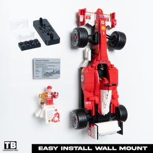 May include: A red and white Lego Ferrari F2004 race car with black tires, displayed with a Lego figurine holding a trophy, a plaque, and mounting hardware. The text "EASY INSTALL WALL MOUNT" is at the bottom.