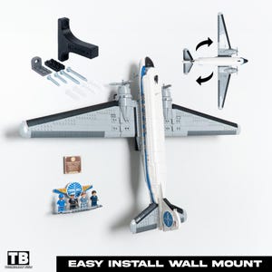 May include: A model airplane in white and grey, mounted on a white wall, with a black mounting bracket and fixings. The image also shows a small Pan Am display with miniature figures and a plaque. The text "EASY INSTALL WALL MOUNT" is at the bottom.