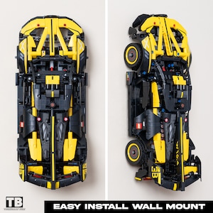 May include: A black and yellow LEGO Technic model car with a wall mount. The car is displayed in two positions, one with the front facing the viewer and the other with the side facing the viewer. The wall mount is a black plastic bracket with a metal hook.
