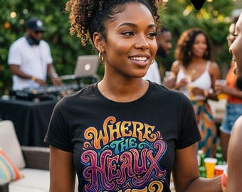 May include: A black short-sleeved t-shirt featuring a colorful graphic print with the text "WHERE THE HEAUX ZAT?" in a stylized, swirling font. The design incorporates shades of orange, purple, blue, and pink, set against a solid black background.